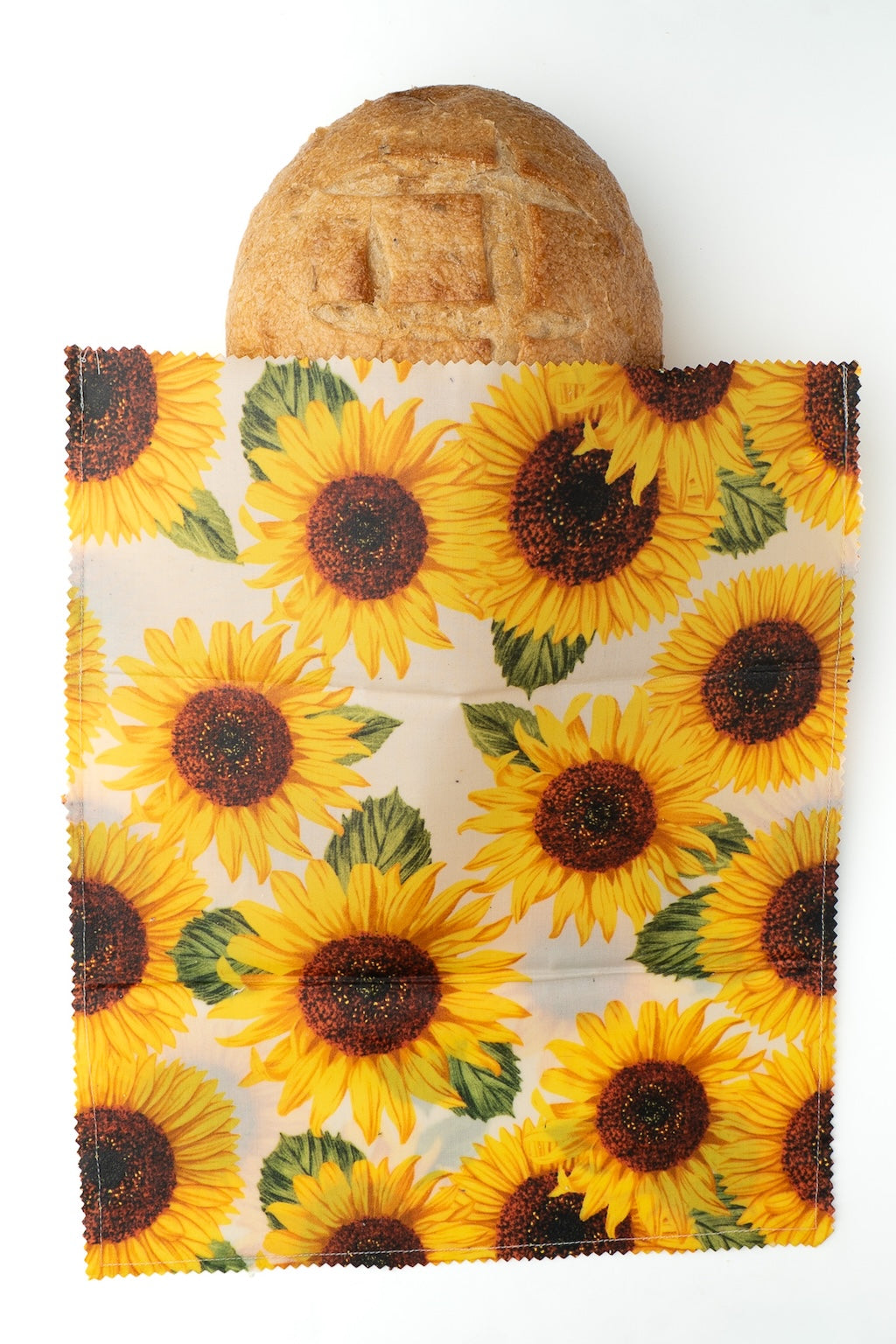 Sunflower-patterned beeswax wrap with a loaf of bread inside on a white background
