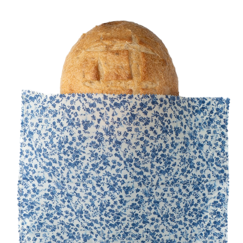 Loaf of bread wrapped in blue floral-patterned beeswax wrap on a white background